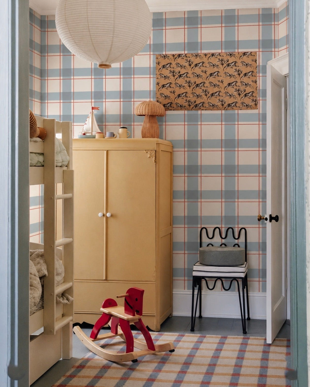 Montaje del papel mural Check Vincent en un dormitorio infantil con litera de madera clara, armario amarillo y cuadros azul grisáceo, crudo y rojo teja.